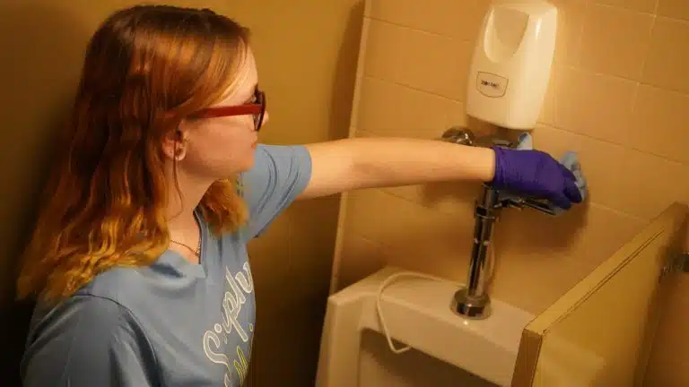 Simply Maid cleaner wiping a soap dispenser and wall in purple gloves