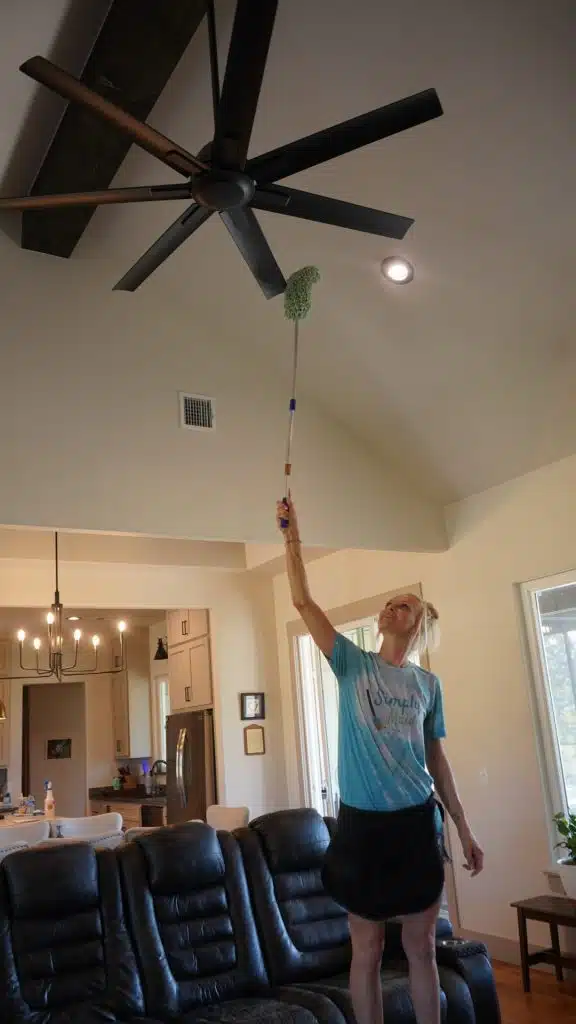 Simply Maid cleaner dusting a high ceiling fan with an extension duster
