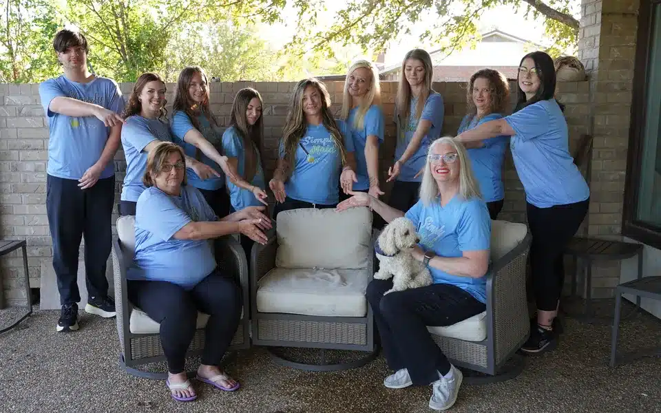 The Simply Maid team on a patio pointing to an empty chair to welcome a new team member, October 2026